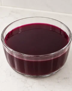 Fresh-pressed Concord grape gelatin mixture in the same plain round glass mold used to form the finished jello