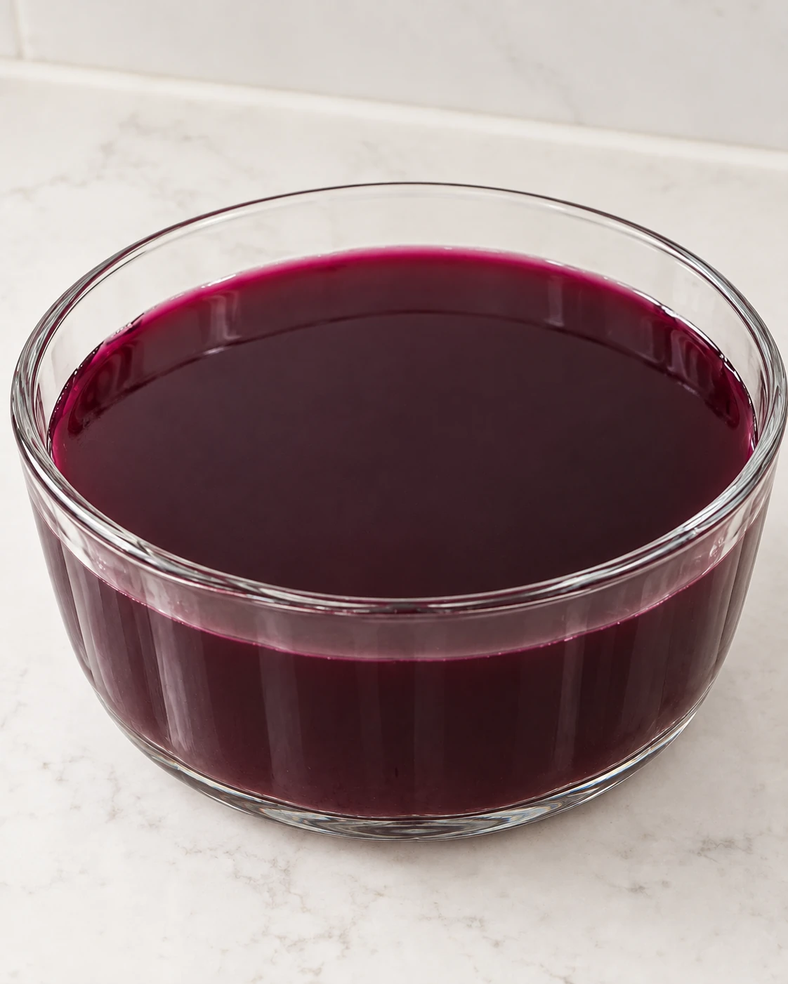 Fresh-pressed Concord grape gelatin mixture in the same plain round glass mold used to form the finished jello