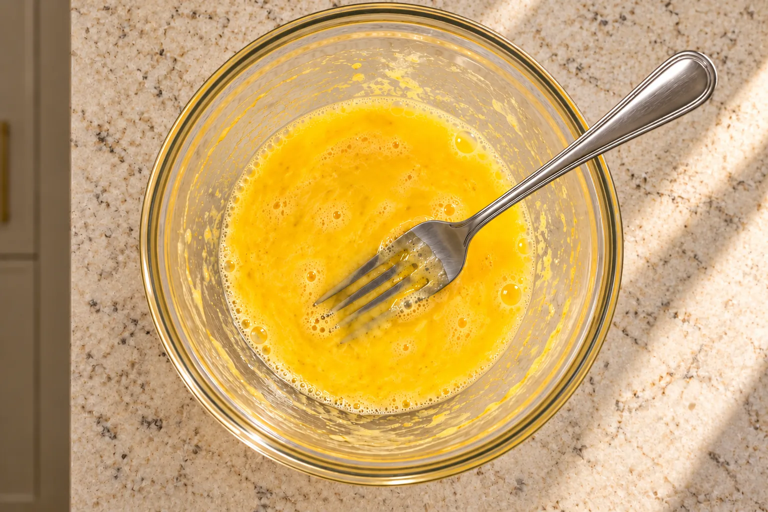 Two lightly beaten eggs in a glass bowl with a fork coated in egg
